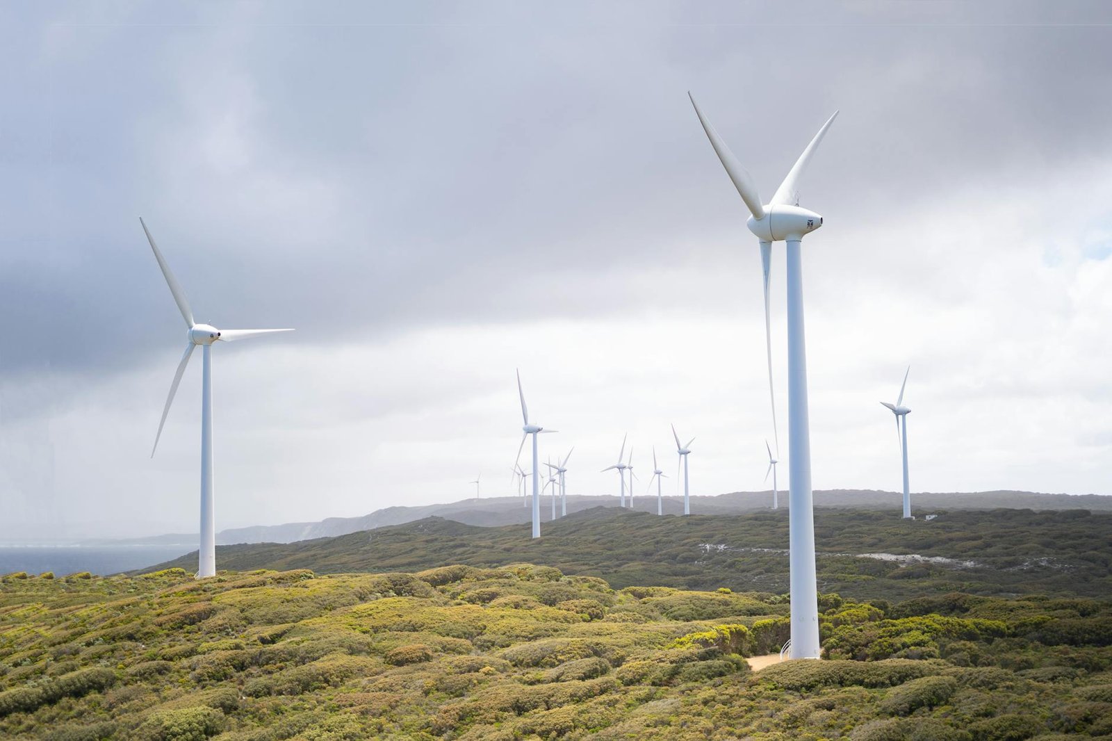 Resources Majestic wind turbines harnessing energy in a vast green landscape under cloudy skies.